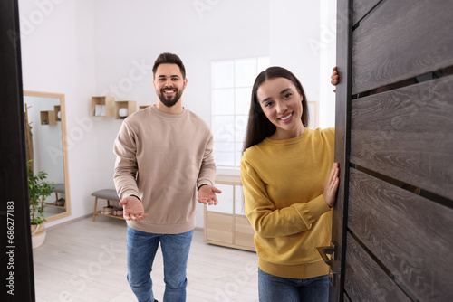 Happy couple welcoming at home. Invitation to come indoors