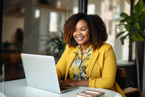 plump,plus-size,black woman,manager, in yellow business clothes sitting at a desk with a laptop in a modern office,diversity concept