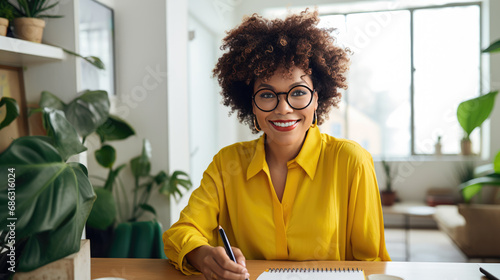Woman with curly hair and glasses is writing in a notebook at a home office