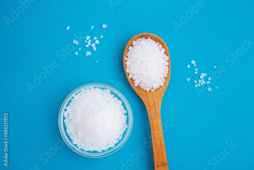 Wooden spoon with salt and glass bowl on the blue background