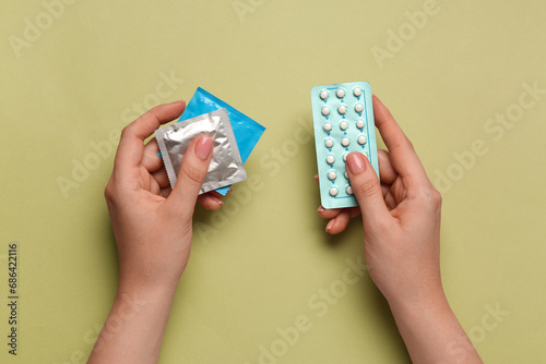 Woman with condoms and contraceptive pills on olive background, top view. Choosing birth control method