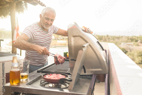 Mature man grilling steaks on a gas grill on his penthouse terrace