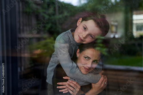 Loving son embracing mother while standing at home seen through window