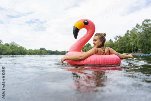 Young woman floating on a lake in a pink flamingo floating tire