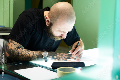 Tattoo artist designing motif on light table in studio