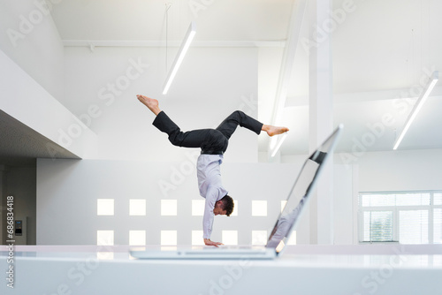 Businessman doing a handstand at laptop in office