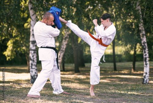 Teenage boy with instructor practicing karate at summer park