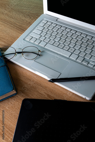 white laptop on a wooden table with blue agenda and graphic tablet, glasses on a white laptop, work and study space, office