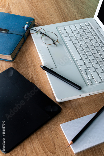 white laptop on a wooden table with blue agenda and graphic tablet, glasses on a white laptop, work and study space, graphic design