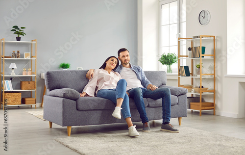 Young family couple spending time at home. Happy, relaxed man and woman sitting together on a comfortable sofa in a modern living room interior in their house or apartment