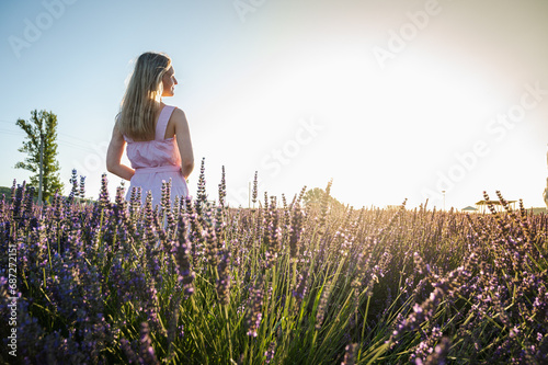 Portrait of a girl in a white summer dress walking through lavender fields, looking from the back to us. Lavender fields near Lviv, Ukraine. Blooming lavender in summer. Sunset. Selective focus