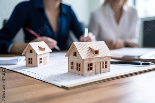 Happy young clients signing mortgage agreement for new home with real estate agent or realtor. Concept of home loan and buying own property. Close up of miniature houses