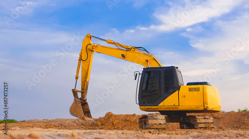 Yellow excavator is leveling the ground for construction area of industrial building in construction site against blue sky background