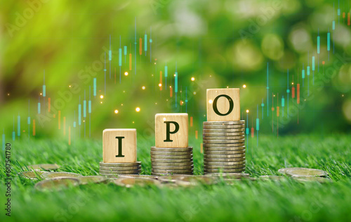 Rows of money coins stacks with IPO word on wooden cube and candlestick charts in the garden sunshine day background for Initial Public Offering, Increased investment concept, economic concept.
