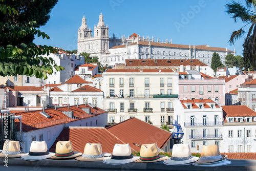 Close up of several typical Portuguese straw hats displayed on a wall in Alfama neighborhood, Lisbon, Portugal with colorful houses and Monastery of São Vicente de Fora in background