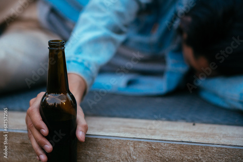 Focus on beer bottle, Asian sleepy drunk man holding beer bottle and lying on floor after nightlife party event, concept for birthday, New Year, disappointed work, sadness or heartbroken