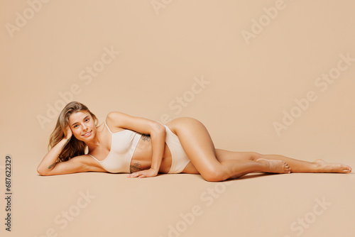 Full body young nice satisfied happy lady woman with slim body perfect skin wearing nude top bra lingerie lay down looking camera isolated on plain pastel beige background. Lifestyle diet fit concept.