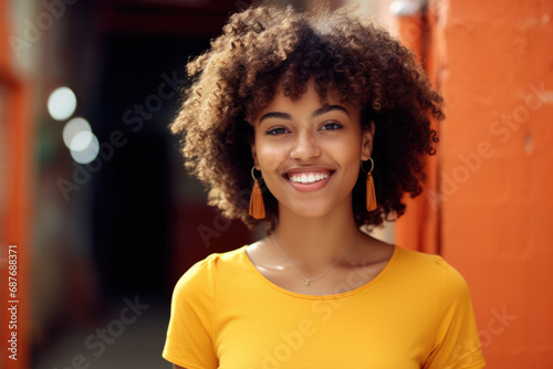 A woman wearing a yellow shirt and earrings smiles for the camera