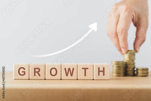 Business success growing growth increase up concept. Wooded cube block with word GROWTH and increasing graph, blurred hand arranged stack of coins