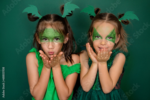 Children in the guise of a dragon - the symbol of 2024, I'm blowing kisses. Girls in green outfits on a studio background