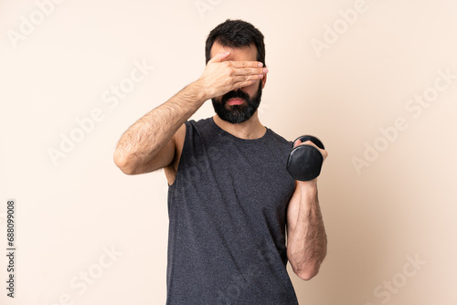 Caucasian sport man with beard making weightlifting over isolated background covering eyes by hands. Do not want to see something