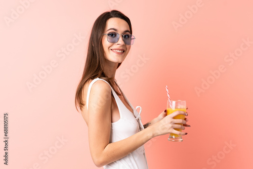 Young woman over isolated pink background in swimsuit and holding a cocktail