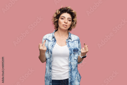 Portrait of rude impolite serious woman with curly hairstyle wearing blue shirt standing with middle fingers, arguing with somebody. Indoor studio shot isolated on pink background.