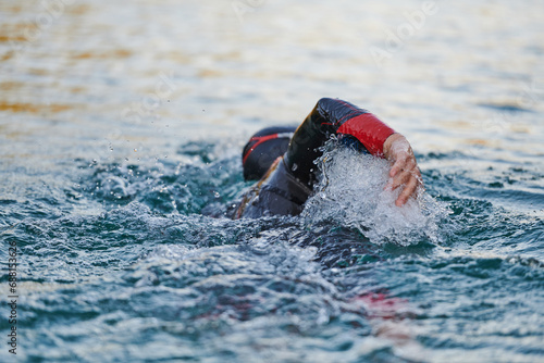 Triathlon athlete swimming on lake in sunrise wearing wetsuit