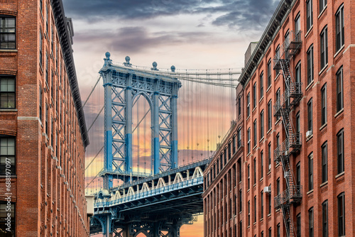 Iconic view of Manhattan Bridge, New York City, USA seen from Washington Street in Dumbo (Down Under the Manhattan Bridge Overpass), Brooklyn with clouds coloring orange during sunset