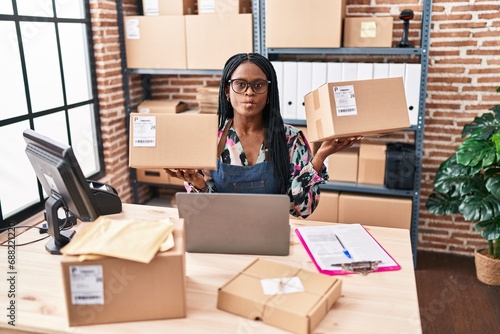 African woman with braids working at small business ecommerce holding packages making fish face with mouth and squinting eyes, crazy and comical.
