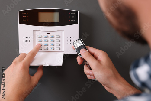Man checking home security alarm system with key fob near gray wall, closeup