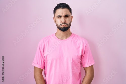 Hispanic young man standing over pink background puffing cheeks with funny face. mouth inflated with air, crazy expression.