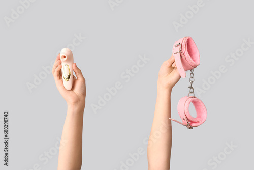 Female hands with sex toys on grey background, closeup