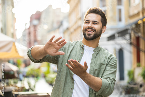 Cheerful rich bearded young man showing wasting throwing money around hand gesture, more tips earnings, big profit, win lottery, share, celebrate outdoors. Caucasian guy standing in urban city street