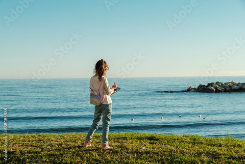 Playa de Pedregalejo, Málaga, niña seis años en el césped, frente al mar, escribiendo en su diario, día soleado, cielo sin nubes