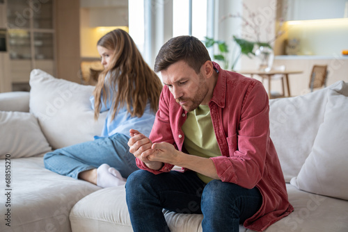 Indifferent uncaring man sitting on sofa, demonstratively examining hands, neglecting wife, and offended upset desperate woman after quarrel, argue, disagreement. Family crisis, conflict, gaslighting