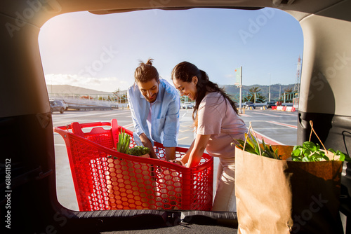 Couple loading groceries from cart to car trunk