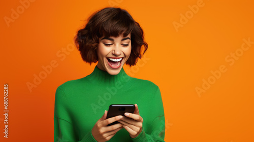 Happy smiling young woman is using her smartphone against orange background