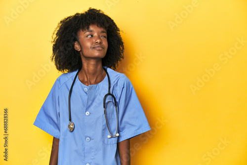 Young African-American nurse in studio with yellow background dreaming of achieving goals and purposes