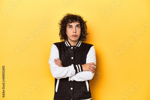 Curly-haired Caucasian woman in baseball jacket tired of a repetitive task.