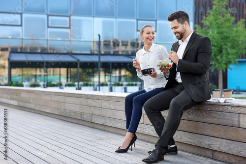 Smiling business people eating from lunch boxes outdoors. Space for text