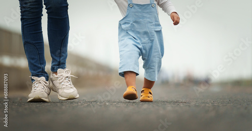 close up leg of infant baby walking on path with mother helping