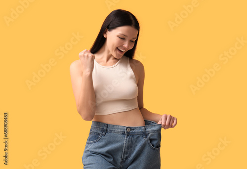 Beautiful young happy woman in loose jeans on yellow background. Weight loss concept