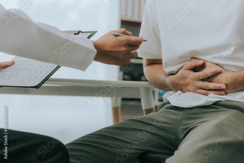 Crohn's disease or ulcerative colitis concept. Doctor counseling male patient with abdominal pain in hospital examination room