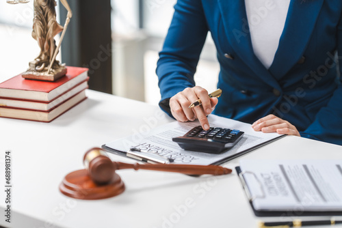 Close up of a lawyer calculating expenses, with a legal contract, gavel, and law books on the table.