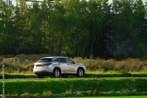 Speeding on a road in a sporty luxury car with a sunset and forest background. Sophisticated expensive car on the road. Premium and Elegant luxurious car on the highway.