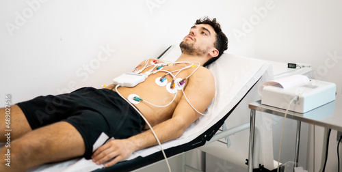 A young man undergoes an electrocardiogram test to diagnose heart disease in a hospital ward. electrocardiograph. Concept of ECG or EKG, electrocardiogram in young people.