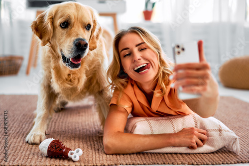 Fun together. A happy woman is taking a selfie with her cheerful pet, who has a funny expression on his face, and they are lying on the living room floor and making funny faces.Emotional connection.