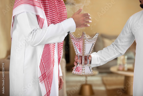 An Arab man holds a censer for his guesr perfumes him with it
