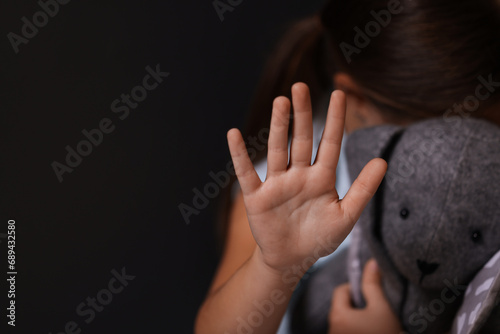 Child abuse. Little girl with toy bunny doing stop gesture on dark background, selective focus. Space for text